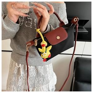 Detail of black nylon handbag with brown leather trim and yellow duck charm on model