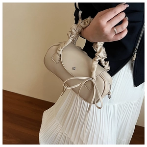 Detail der cremefarbenen Zylindertasche mit gerafftem Griff und eleganter Schleife