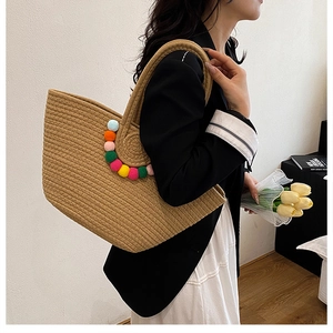 Vue détaillée du sac cabas tissé orné de pompons colorés et texture naturelle