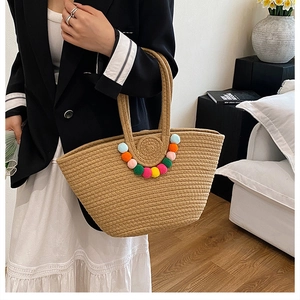 Détail d'un sac cabas en paille avec pompons colorés et design de texture tissée