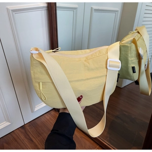 Detail of light yellow nylon crescent crossbody bag featuring zipper pocket and buckle strap