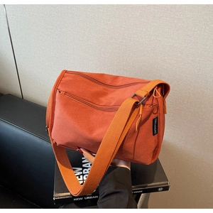 Detail view of orange canvas crossbody bag with multiple zippers and wide fabric strap