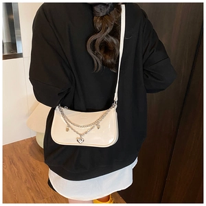 Detail of cream patent leather baguette bag featuring silver chains and heart pendant