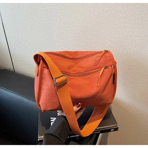Detail view of orange nylon crossbody bag featuring multi-zipper layers and wide strap