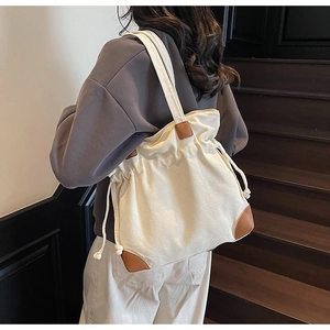 Canvas drawstring tote bag with brown leather accents worn by a model in a retro hallway