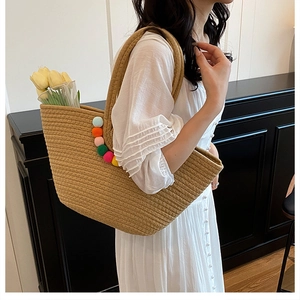 Vue détaillée du sac cabas en paille avec pompons colorés et texture tissée