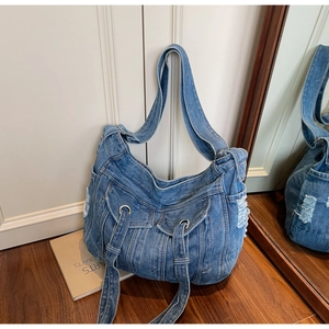 Detailed texture of blue denim crossbody bag with vintage distressed frayed edges and metal eyelets