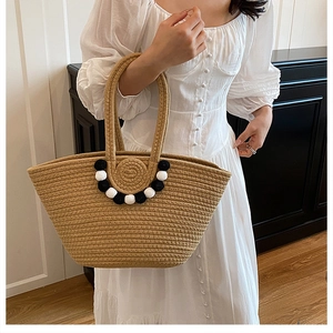 Détail du sac cabas en paille tissée avec pompons noirs et blancs et doubles poignées