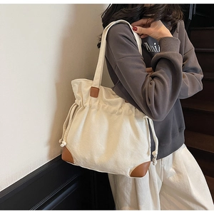 Detail view of canvas tote bag with brown leather corner guards and drawstring closure