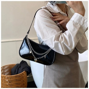 Detail of black patent leather shoulder bag with silver chains and heart charms