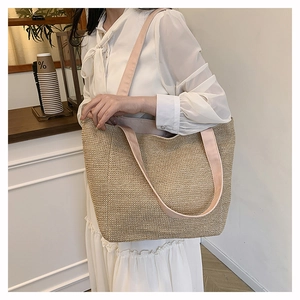 Detail of the woven straw tote bag featuring wide pink fabric shoulder straps for women