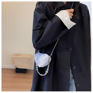 Iridescent heart-shaped mini crossbody bag with silver chain strap shown on navy blue coat