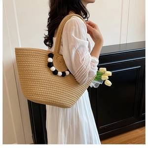 Sac fourre-tout en paille avec pompons et texture tissée porté par un mannequin