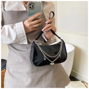 Detail of glossy black patent leather bag with silver heart and lock chain pendants