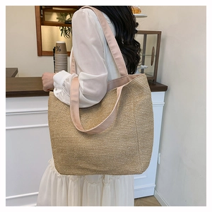 Detail of woven straw tote bag with pink fabric straps shown in a lifestyle cafe setting