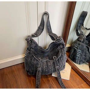 Detail of distressed dark denim crossbody bag with multiple pockets on wooden floor