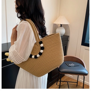 Gros plan du sac cabas en paille kaki montrant la texture et les pompons bicolores