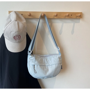 Detail of light blue nylon crescent crossbody bag hanging on a wooden hook