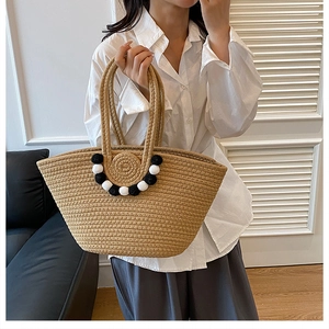 Détail d'un sac cabas en paille tressée avec pompons décoratifs bicolores et texture