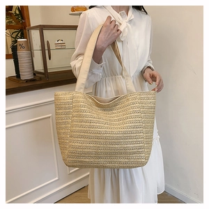 Detail of woven straw tote bag with wide canvas shoulder straps on a white dress model