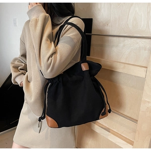 Detail of black canvas tote bag with brown leather trim and drawstring closure