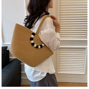 Détail du sac cabas tissé montrant des pompons noirs et blancs et texture en corde