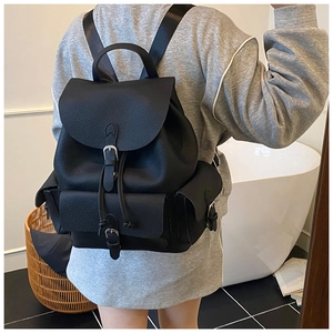 Detail of black lychee grain leather backpack featuring dual buckle straps and drawstring