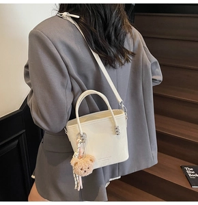 Dettaglio borsa a secchiello bianca con texture martellata e ciondolo a forma di orso