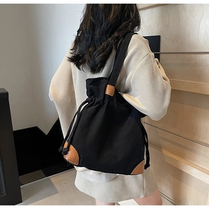 Detail view of black canvas shoulder bag featuring brown leather reinforcement and drawstring