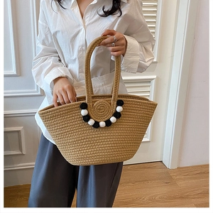 Détail du sac cabas en paille tissé avec pompons noir et blanc pour look de plage d'été