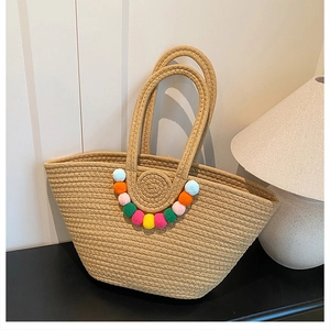Détail du sac cabas en paille tissé à la main avec pompons colorés sur une table épurée