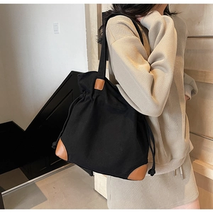 Detail of black canvas tote bag with drawstring closure and brown leather accents