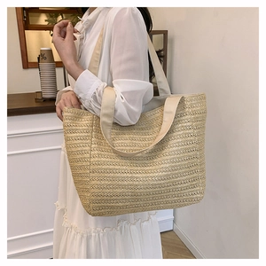 Close-up of a woven straw tote bag with fabric straps worn by a model in a cafe