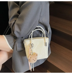 Dettaglio borsa a secchiello crema con pelle effetto marmo e ciondolo a forma di orsetto