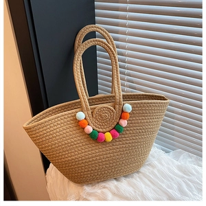 Gros plan du sac en paille avec pompons colorés sur un tissu blanc texturé