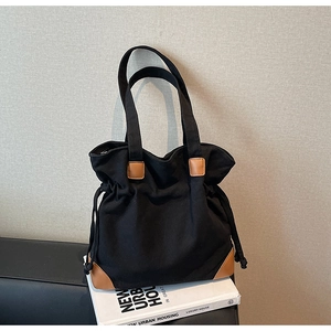 Detail of black canvas tote bag with brown leather trim and side drawstring accents