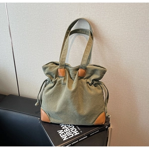 Close-up of olive canvas tote with drawstring closure and brown leather corner accents