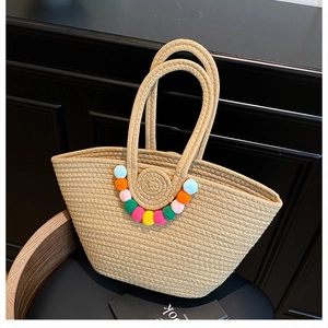 Détail d'un sac cabas en paille tissé main avec pompons colorés et anses rondes