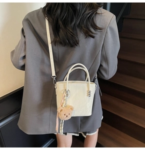 Close-up of white leather bucket bag with brand embossing and cute bear charm pendant