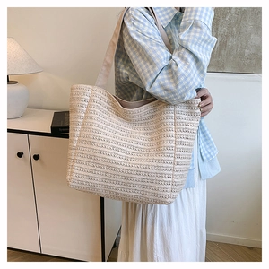Detail of beige woven straw tote bag featuring intricate texture and wide fabric strap