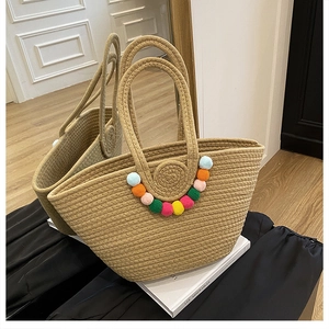 Détail d'un sac cabas en paille avec pompons colorés et texture tissée fine