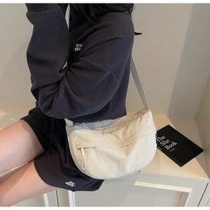 Detail of a cream nylon crescent bag showing the adjustable strap and zip pocket