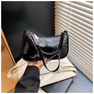 Detail of minimalist black patent leather square bag with silver chain and zip closure