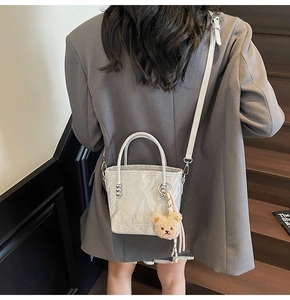 Sac seau argenté avec texture plissée et breloque ours en peluche sur l'épaule