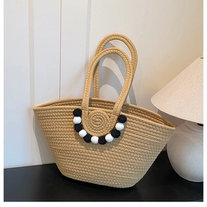 Détail d'un sac cabas en paille avec pompons décoratifs contrastés noirs et blancs