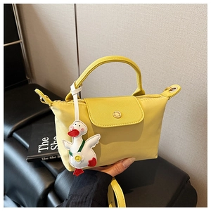 Detail of yellow nylon handbag with leather flap and cute white cartoon duck pendant