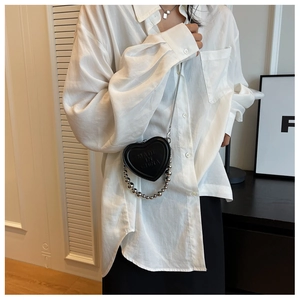 Close-up of heart-shaped black leather mini bag with silver bead chain on white shirt