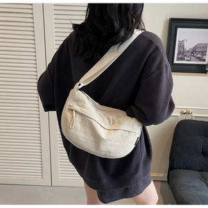 Detail of a minimalist beige nylon crescent crossbody bag worn over a purple sweatshirt