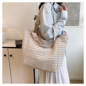 Detail of woven straw tote bag texture and wide strap on shoulder of a model