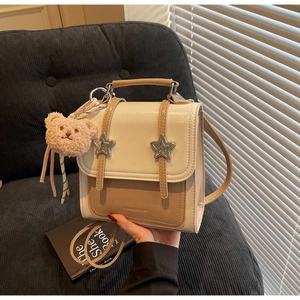 Detail of a retro two-tone square bag with silver star buckles and a plush bear charm